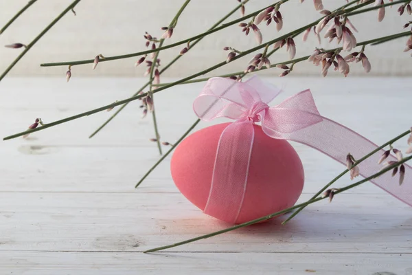 Uova di Pasqua rosa con un nastro sotto genista fioritura o scopa su un tavolo di legno verniciato bianco, spazio copia — Foto Stock