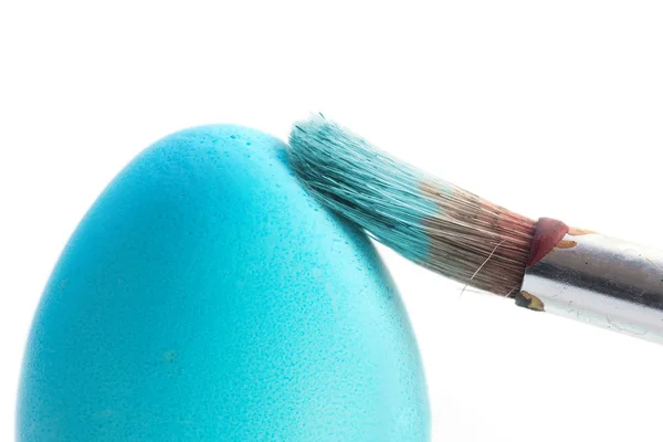 Escova áspera está pintando um frágil ovo de Páscoa com uma cor azul-turquesa, macro tiro isolado em um fundo branco, foco selecionado na escova — Fotografia de Stock