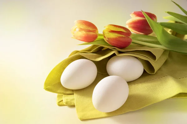 Ovos de Páscoa brancos em um guardanapo verde e tulipas vermelhas, cartão de felicitações de férias com espaço de cópia — Fotografia de Stock