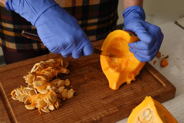 Preparación de la calabaza para cocinar, mujer con guantes de goma azul quita las semillas de la fruta —  Fotos de Stock