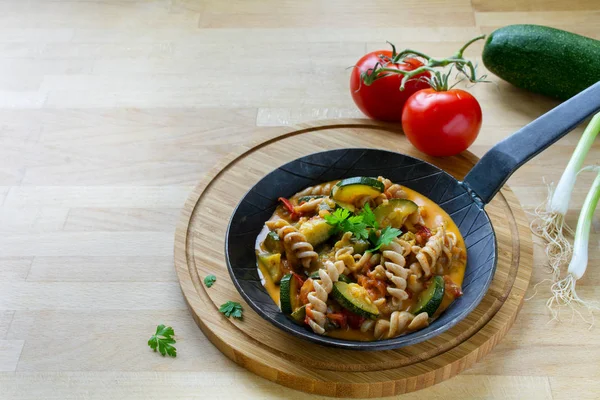 Ολικής αλέσεως ζυμαρικά με κολοκυθάκια και ντομάτα λαχανικά σε μια κατσαρόλα σε ένα πλοίο ξύλινη κουζίνα, Υγιεινή Χορτοφαγική διατροφή γεύματος, γενναιόδωρη αντίγραφο χώρου, επιλεγμένο εστίαση — Φωτογραφία Αρχείου