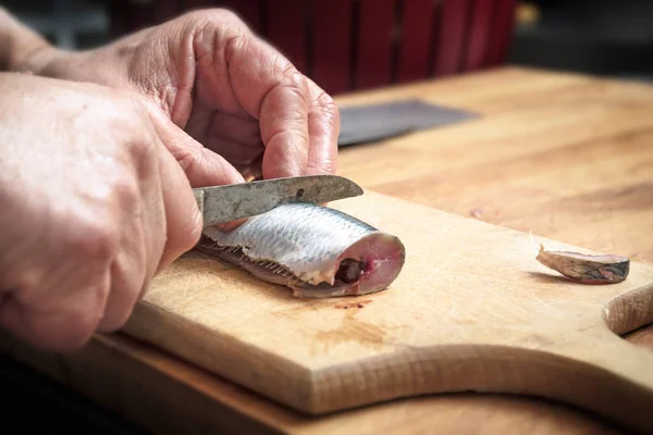 Männliche Hände bereiten einen Heringsfisch mit einem Küchenmesser auf einem hölzernen Schneidebrett zu, kopieren Raum — Stockfoto