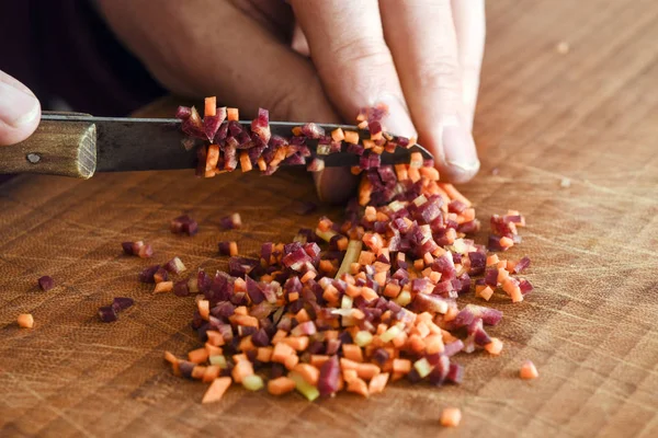 Handen snijden van groenten in kleine blokjes op het bord van een houten keuken, voorbereiding voor het koken, close-up — Stockfoto