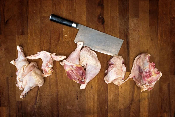 Pezzi di carne di un pollo crudo e una mannaia di cucina su un tavolo rustico di legno, vista di angolo alta dall'alto, copiano lo spazio — Foto Stock