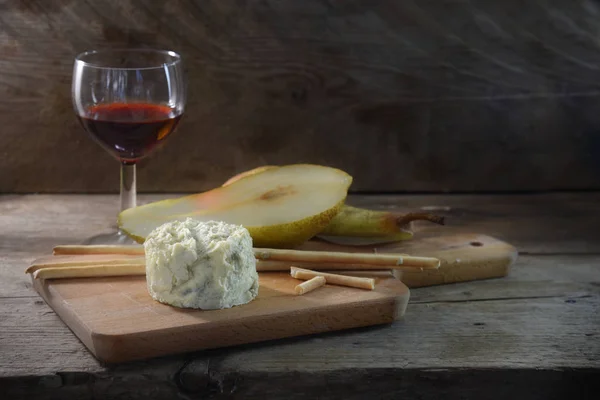 Creamy blue stilton cheese, port wine, pear and some nibble sticks on a cutting board against a dark rustic wooden background, copy space — Stock Photo, Image
