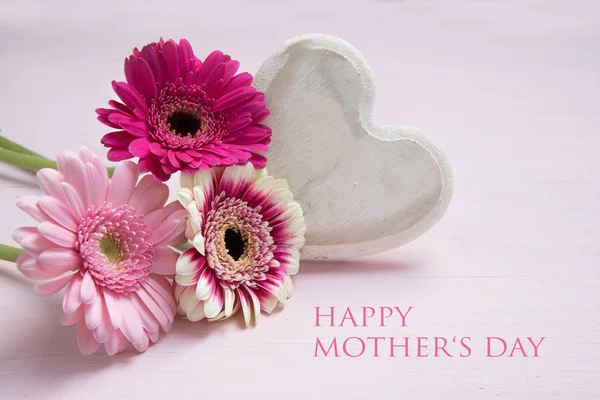 Pink flowers and a white painted wooden heart on a pastel colored background, love symbol with text Happy Mother's Day, copy space — Stock Photo, Image