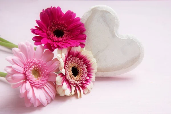 Roze bloemen en een wit geschilderde houten hart op een pastel gekleurde achtergrond, symbool van de liefde voor de dag van Valentijnskaarten of moeders, kopiëren ruimte — Stockfoto