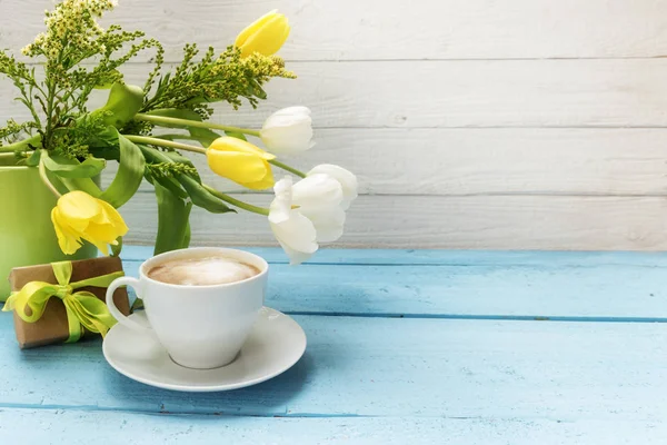 Taza de café, flores de tulipán amarillo y blanco en un jarrón verde y un pequeño regalo en madera turquesa, fondo de madera blanca con espacio para copiar —  Fotos de Stock