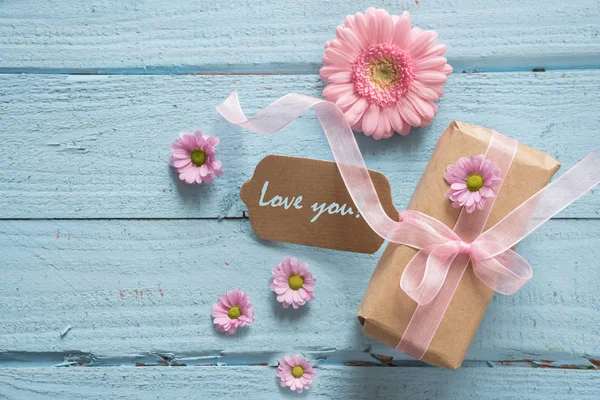 Presente em papel marrom e rosa cabeças de flores em um fundo de madeira azul pastel com espaço de cópia, texto Amo você — Fotografia de Stock