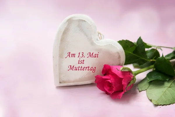 Corazón de madera y una rosa sobre un fondo rosa, texto alemán Am 13. Mai ist Muttertag, que significa 13 de mayo es el día de la madre — Foto de Stock