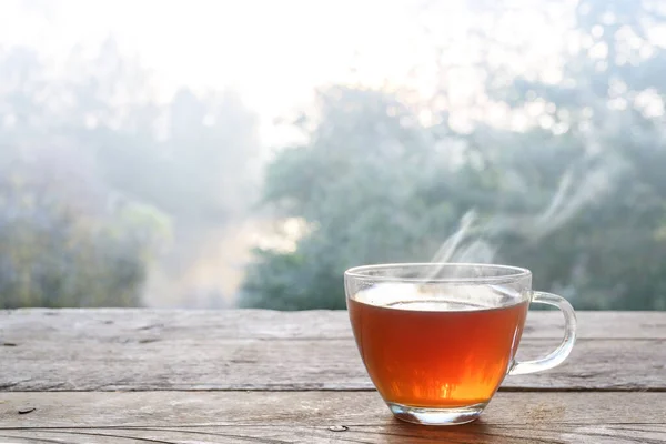 Hot steaming tea in a glass cup on a rustic wooden outdoor table on a cold foggy winter day, copy space — Stock Photo, Image