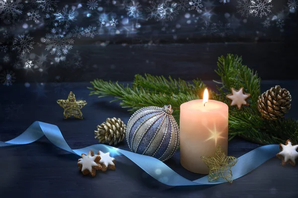 Bougie ardente et boule de Noël bleue, entourée de branches de sapin, d'étoiles de cannelle et d'un ruban sur un fond de bois bleu nuit avec quelques flocons de neige, décoration festive avec espace de copie — Photo