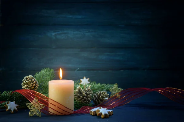 Decoração de Natal com uma vela branca acesa, ramos de abeto, estrelas de canela e fita vermelha contra um fundo de madeira azul escuro, grande espaço de cópia — Fotografia de Stock