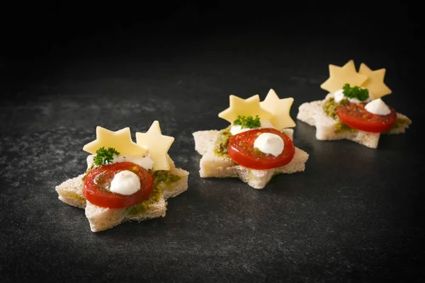 Creative christmas canapes in a row with tomato, pesto and cheese in star shape on a dark stone slab with copy space — 스톡 사진