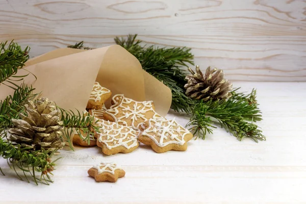 Пряничное печенье на Рождество выпадает из бумажного пакета, ели ветки и шишки сосны на белом окрашенном деревенском фоне дерева, копировальное пространство — стоковое фото