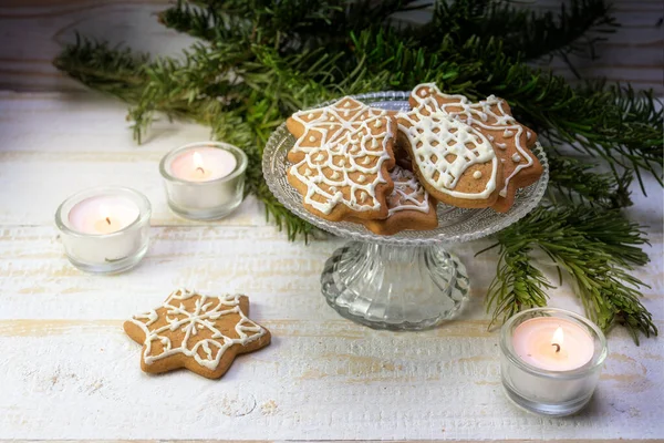 Lebkuchen-Weihnachtsgebäck auf einer festlichen Glasschüssel mit brennenden Kerzen und Tannenzweigdekoration auf einem weiß bemalten Holztisch, Kopierraum, ausgewählter Schwerpunkt — Stockfoto