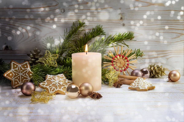 Brennende Kerze mit Weihnachtsdekoration, Tannenzweige, Kugeln, Strohsterne und Lebkuchen auf rustikalem Holz, verschneite Bohème-Lichter, Kopierraum — Stockfoto