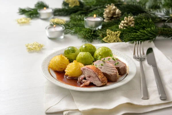 Petto d'anatra con cavoletti di Bruxelles, patate duchessa e salsa come cena festiva, servito su un tavolo di legno bianco con rami di abete candele e decorazione natalizia — Foto Stock