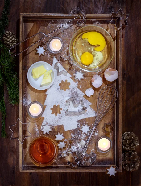 Christmas bakery, fir tree shape powdered from flour, ingredients for cookies, baking utensils and burning candles on a dark wooden tray, flat lay, high angle view from above — Stock Photo, Image