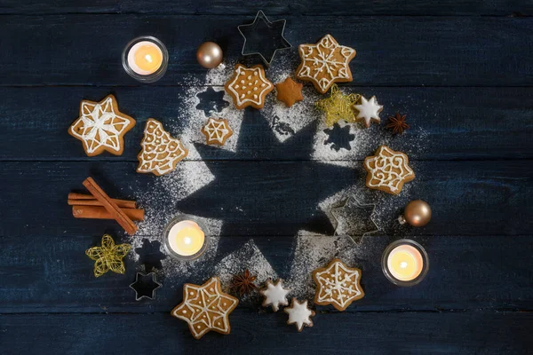 Weihnachtliches Arrangement mit Lebkuchen, Gewürzen und brennenden Kerzen auf einem Stern aus Puderzucker auf dunkelblauem Holzgrund, Kopierraum, Blick von oben — Stockfoto