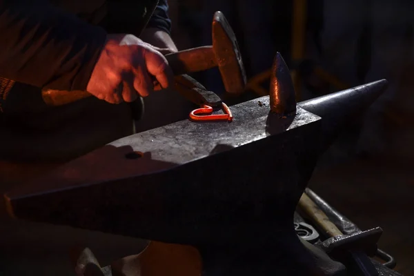 Blacksmith forges a hot glowing iron heart with a hammer on the anvil, symbol of eternal love, dark background, copy space — Stock Photo, Image