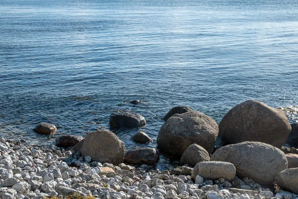 Raue Meeresküste mit Kieselsteinen und großen Steinen in blauem Wasser, Kopierraum — Stockfoto