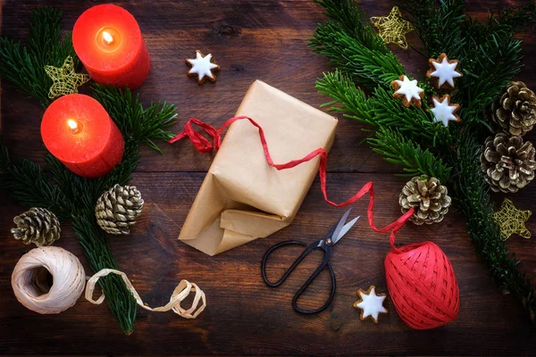 Karácsonyi ajándék csomagolása sötét rusztikus fára, égő vörös gyertyákkal, fenyőágakkal, fahéjas csillagokkal és karácsonyi dekorációval, felülnézetből. — Stock Fotó