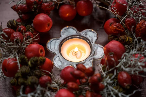 Kleine krans met rozenbottels en rode appels rond een brandende kaars als tafeldecoratie in de herfst, advents- en kersttijd — Stockfoto