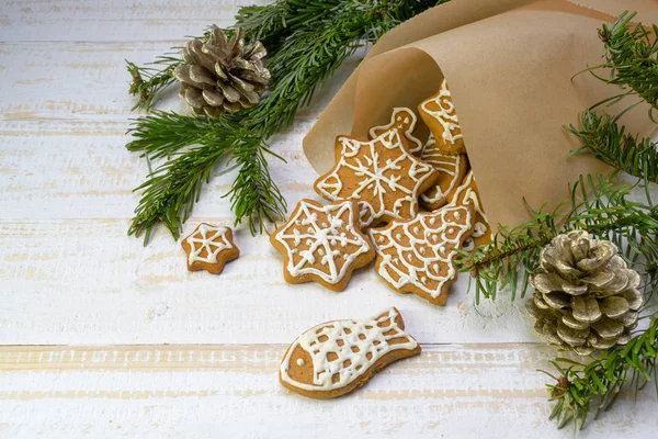 Домашнее пряничное печенье на Рождество в бумажном пакете, еловые ветки и сосновые шишки на белом покрашенном деревянном столе, место для копирования — стоковое фото