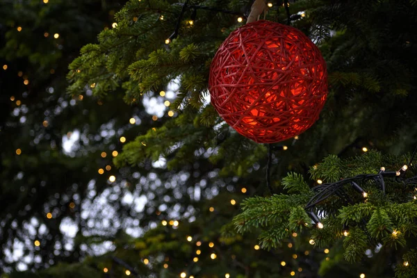 Красный Рождественский шар из веревки в большой елке с легкой цепью, наружное оформление в праздничный сезон от прихода до Нового года, копировальное место, выбранный фокус — стоковое фото