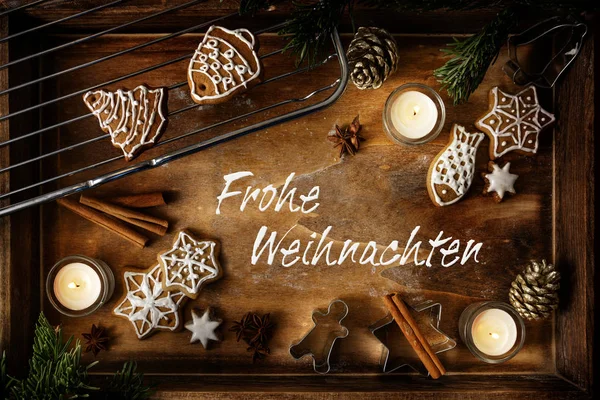 Gingerbread, burning candles and cookie cutters on a dark wooden tray, German text Frohe Weihnachten, meaning  Merry Christmas, flat lay, high angle view from above — Stockfoto