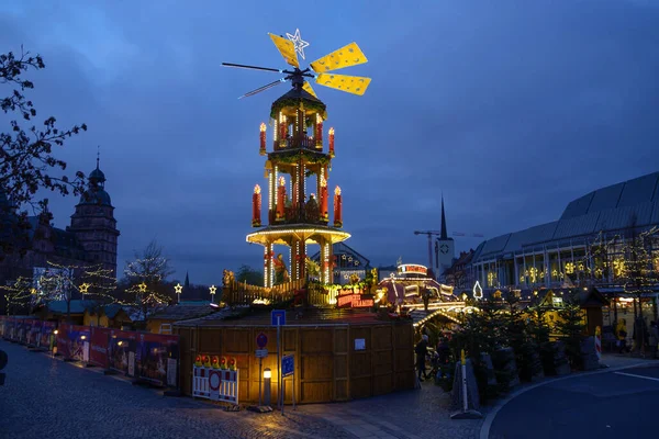 Aschaffenburg - 30. November 2019: Weihnachtspyramide auf dem Adventmarkt auf der Burg johannisburg in Aschaffenburg in der Abenddämmerung vor dunkelblauem Himmel mit Kopierraum — Stockfoto