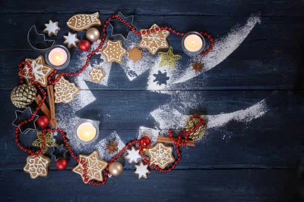 Sternschnuppenform aus Puderzucker, Weihnachtsdekoration, Lebkuchen und brennenden Kerzen auf dunkelblauem Holzgrund, Höhenblick von oben — Stockfoto