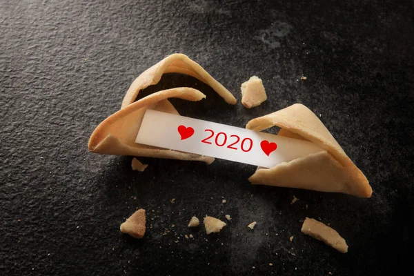 Σπασμένο κινέζικο μπισκότο τύχης με 2020 και κόκκινες καρδιές στο χαρτί γλιστρήσει σε ένα σκοτεινό φόντο με αντίγραφο χώρο, την έννοια του νέου έτους, θέα υψηλής γωνίας από ψηλά — Φωτογραφία Αρχείου