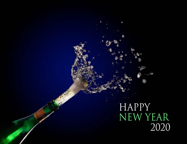 Feliz Ano Novo 2020 texto e uma garrafa de champanhe explodindo e atirando a rolha com salpicos contra um fundo azul escuro, espaço de cópia — Fotografia de Stock