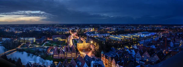 Luebeck, Almanya, 17 Aralık 2019: Holstentor, tarihi Salzspeicher evleri ve Trave nehri ile aydınlık şehir Luebeck 'in hava gece manzaralı panoraması, mavi saatte uzun süreli maruz kalma, — Stok fotoğraf