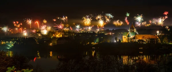 New Year fireworks above the old town of Ratzeburg at night with illuminated cathedral and reflections in the lake, joy for people but panic and fear for animals, panorama view, copy space — Stock Photo, Image