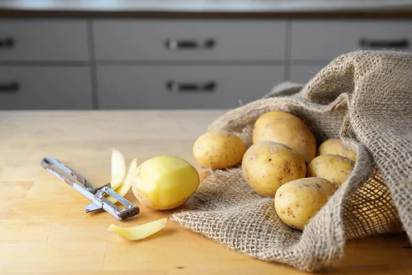 Cartofi într-un sac de pânză, o jumătate decojiți lângă un peeler economic foarte vechi pe o masă de bucătărie din lemn, spațiu de copiere — Fotografie, imagine de stoc