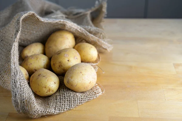 Organic potatoes in an open burlap sack on a wooden kitchen table, copy space — Stock Photo, Image