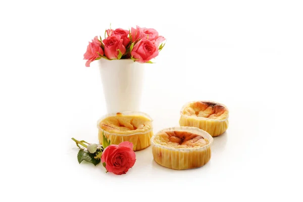 Petits gâteaux ou muffins en caillé faits maison et un vase avec des roses roses isolées avec des ombres sur un fond blanc, espace de copie — Photo