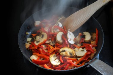 Ocakta siyah bir tavada mantar ve kırmızı dolma biber gibi kızartılmış sebzeler, sağlıklı vejetaryen kavramı.