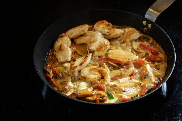 Cooking a creamy chicken ragout with bell pepper and mushroom in a pan on a black stove, copy space — Stock Photo, Image