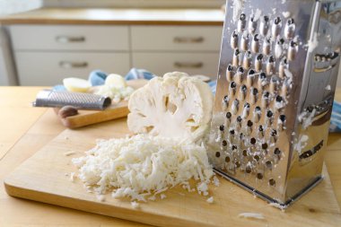 Sağlıklı düşük karbonhidratlı ya da ketojenik diyet öğününü ahşap mutfak atölyesinde pişirmek için pirinç yerine metal rendesi ile rendelenmiş karnabahar.