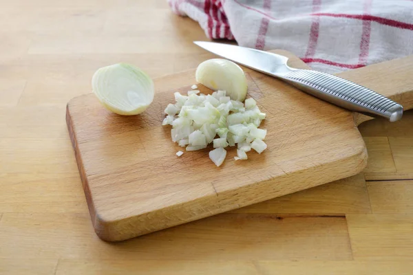 Sekání cibule na malé kostky kuchyňským nožem na dřevěné sekací desce — Stock fotografie