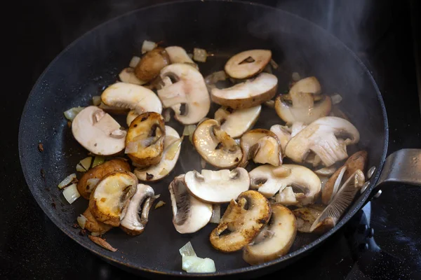 Pieczarki smażone na patelni na czarnej szklano-ceramicznej płycie grzewczej, zdrowa wegetariańska koncepcja gotowania — Zdjęcie stockowe