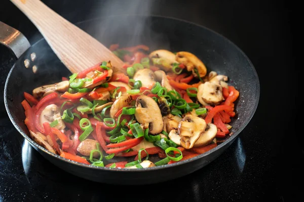 Τηγάνι στον ατμό λαχανικά με κόκκινη πιπεριά, μανιτάρια και φρέσκο κρεμμυδάκι στη μαύρη σόμπα, υγιεινό μαγείρεμα έννοια, αντίγραφο χώρο — Φωτογραφία Αρχείου