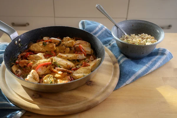 Chicken ragout with bell pepper and mushroom in a cooking pan and cauliflower rice in a bowl on a wooden kitchen table, copy space — Stock Photo, Image