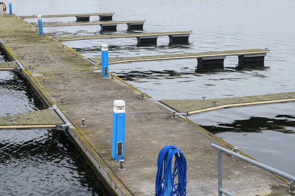 青い電気ボックスとホース、春の冷たい海の水で待っている季節のヨットマリーナと空の桟橋 — ストック写真