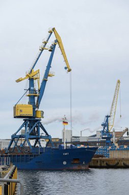 Wismar, Almanya, 2 Şubat 2020: Bulutlu bir gökyüzüne karşı Mecklenburg-Batı Pomerania kentindeki Wismar kentindeki kereste limanında mavi sarı vinç gemisi