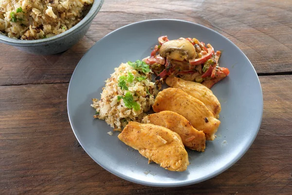 Gesunde Low-Carb-Kost mit Hühnerfilet, Blumenkohl-Reis und Gemüseragout auf blauem Teller auf rustikalem Holztisch — Stockfoto